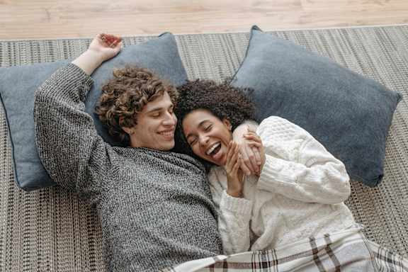 Two people are lying on a couch, one is wearing a grey sweater and the other is wearing a white robe.