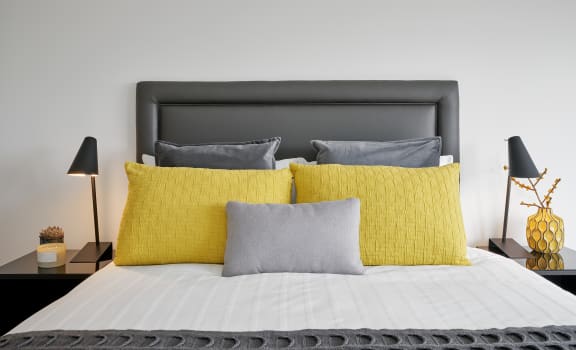a bed with yellow pillows and grey pillows on it