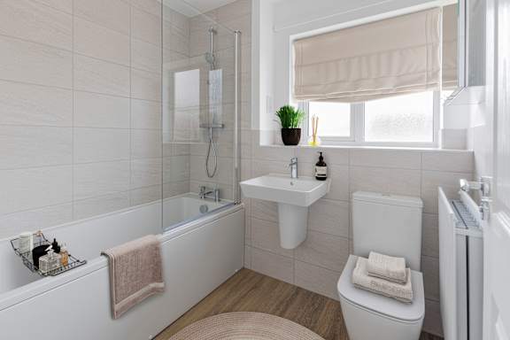 A white bathroom with a towel on the tub and a plant on the window sill.