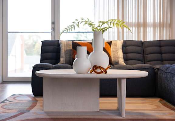 A white vase with a plant sits on a table in front of a couch.