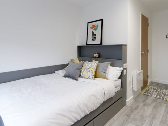 Floor Plan  A bed with a white comforter and two pillows with a grey headboard and a picture frame above it.