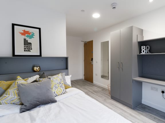 Floor Plan  A bedroom with a bed, a grey headboard, a framed picture on the wall, and a TV on the wall.