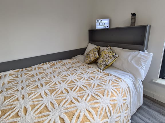 Floor Plan  A bed with a white and yellow patterned blanket and two pillows.