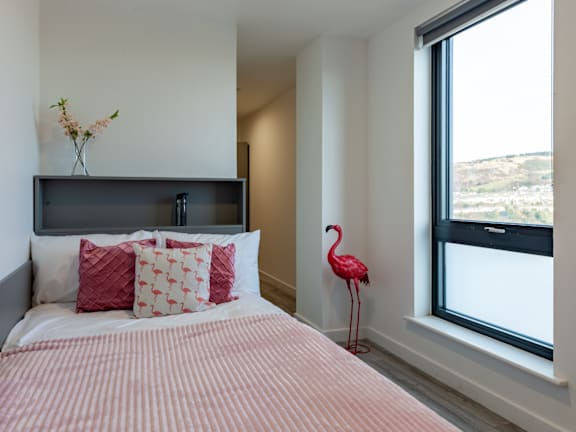 Floor Plan  A bedroom with a bed, pillows, a vase with flowers, and a pink flamingo.