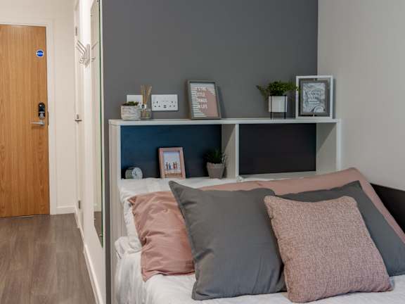 Floor Plan  A bed with pillows and a shelf with picture frames and plants.