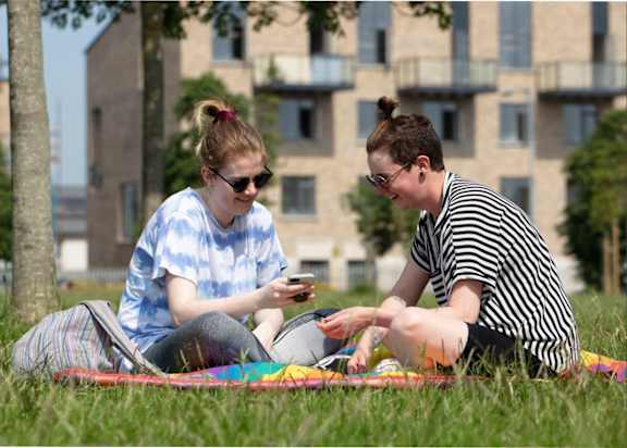 two women sitting on the grass looking at their cell phones