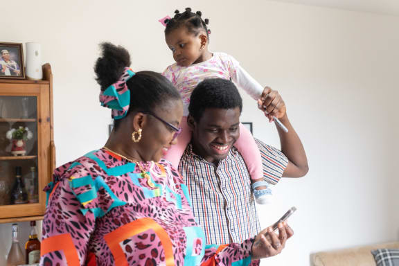 a family of four looking at a cell phone while a child sits on the shoulders