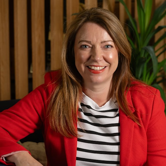 A woman with a red jacket and striped shirt is smiling.
