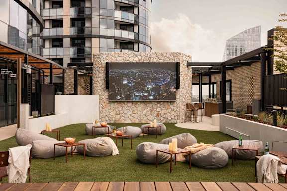 A modern outdoor seating area with bean bag chairs and a large screen on a stone wall.