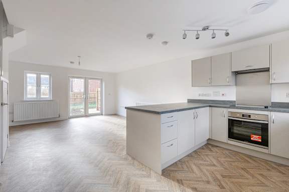 A spacious kitchen with a wooden floor and white walls.