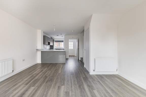 A spacious room with wooden flooring and white walls.