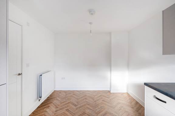 A white room with a wooden floor and a radiator on the wall.