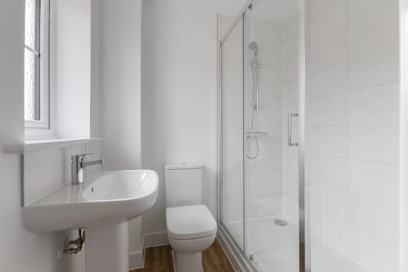 A white bathroom with a sink, toilet, and shower.
