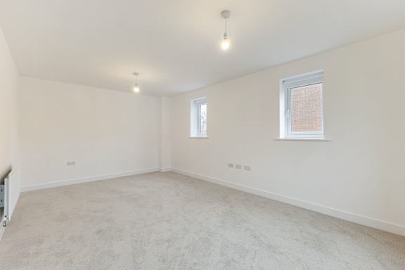 A spacious room with a carpeted floor and two windows.