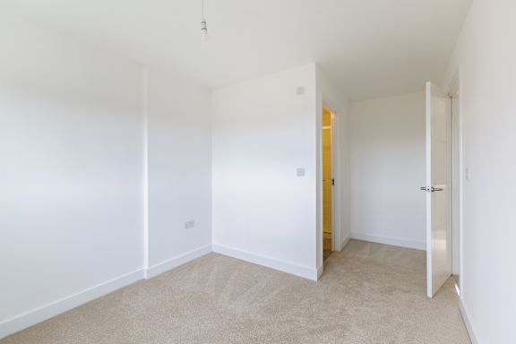 A white room with a carpeted floor and a doorway leading to another room.