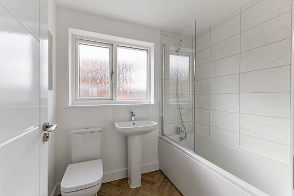 A white bathroom with a toilet, sink, and shower.