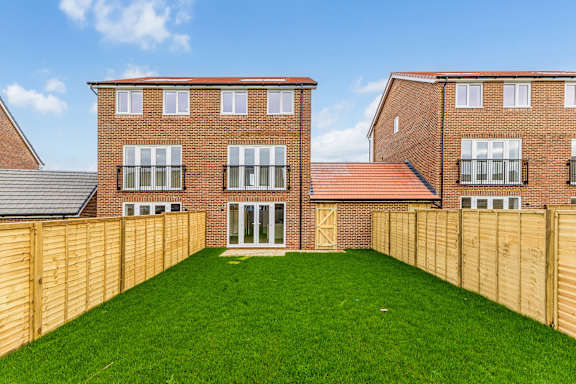 A large grassy yard in front of a red brick house with a wooden fence.