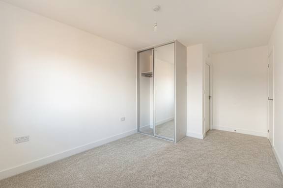 A room with a carpeted floor and a white wall with a mirrored door.