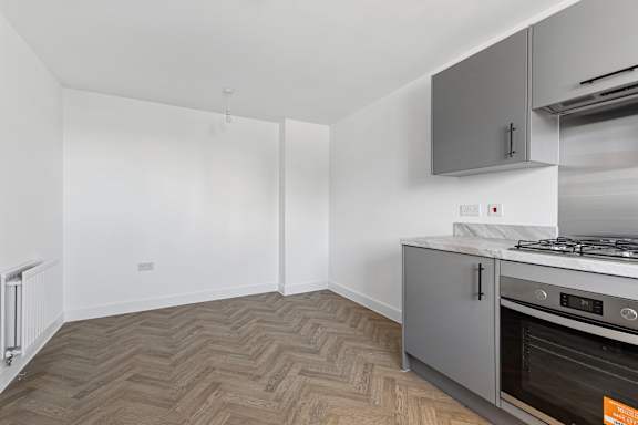 A kitchen with a stove top oven and a wooden floor.