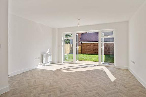 A room with a herringbone patterned floor and a view of a backyard through a sliding glass door.