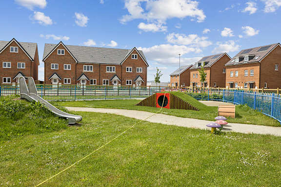 A playground with a slide and a tunnel in front of a row of houses.