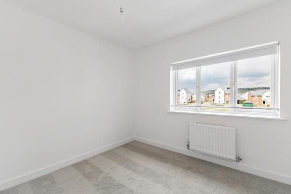 A room with a window showing a view of houses and a radiator on the floor.