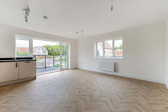 A spacious room with a herringbone parquet floor and a window overlooking a street.