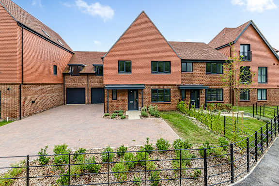 A red brick house with a black fence and a driveway.