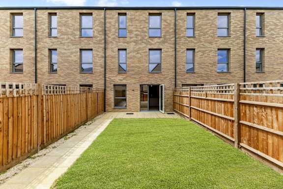 A brown wooden fence surrounds a green lawn in front of a brick building.