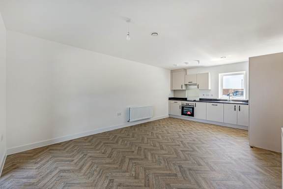 A room with a herringbone patterned floor and a kitchen area in the background.