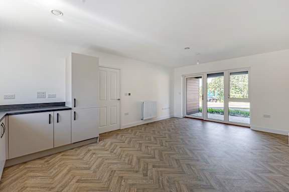 A spacious room with a herringbone parquet floor and a sliding glass door leading to a balcony.