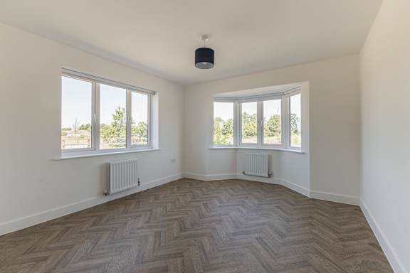 A room with a herringbone patterned floor and two windows.