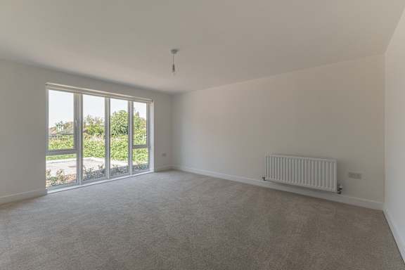 A room with a grey carpet and a white ceiling with a window and sliding doors.