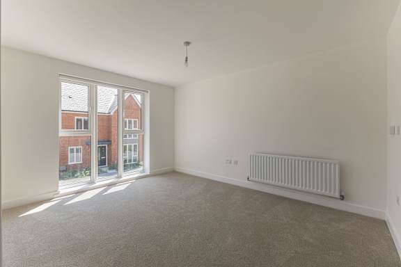 A room with a grey carpet and a white wall with a window and a radiator.