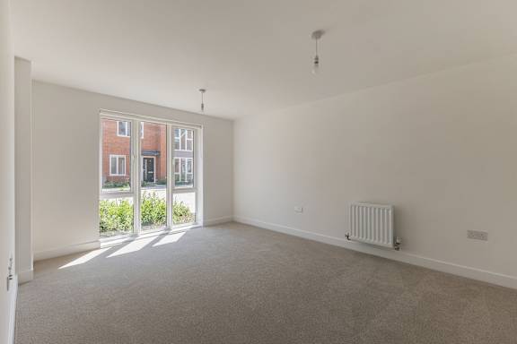 A room with a grey carpet and a white wall with a window and a radiator.