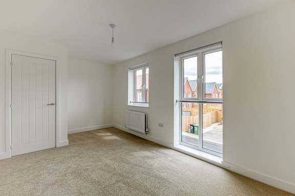 A room with a white door, a window with a radiator beneath it, and a sliding glass door leading to a balcony.