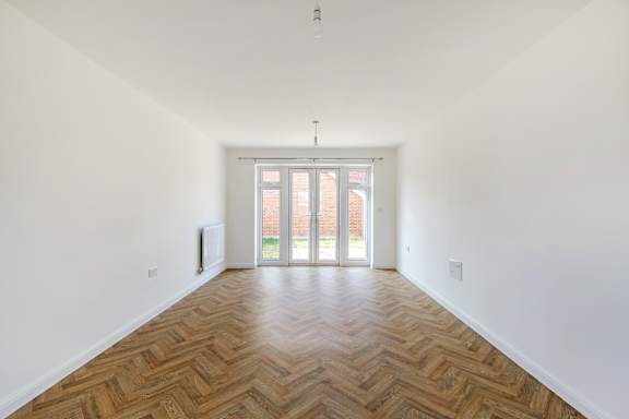 A room with a wooden floor and a white wall with a doorway leading to another room.