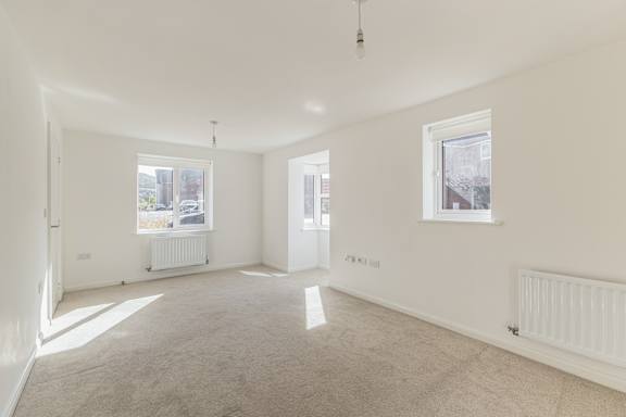 A large, empty room with two windows and a carpeted floor.
