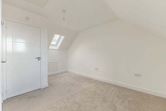 A white door is on the left side of a room with a carpeted floor and a skylight.