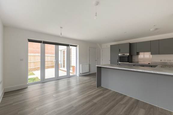 A spacious kitchen and living room with wooden flooring and white walls.