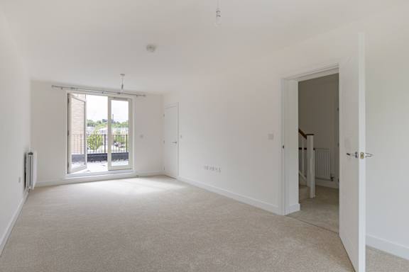 A large, empty room with a sliding glass door leading to a balcony.
