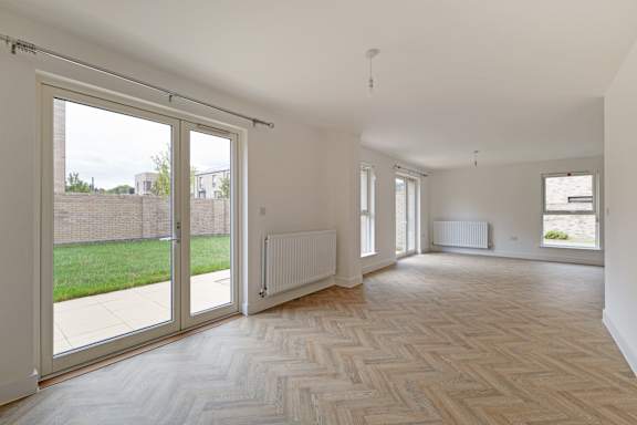 A spacious room with a herringbone parquet floor and sliding glass doors.