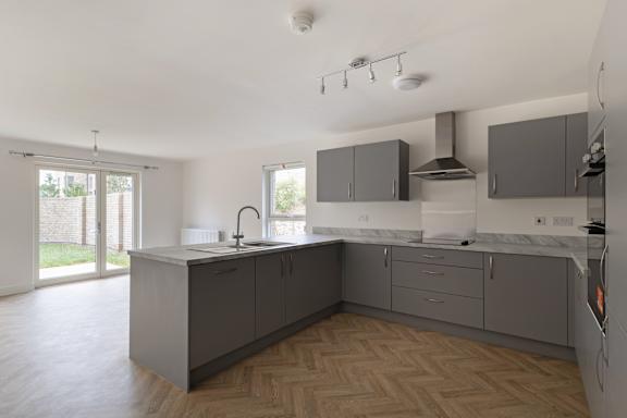 A modern kitchen with wooden flooring and grey cabinets.
