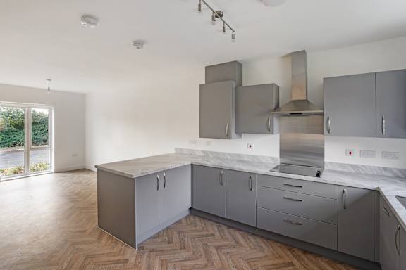A modern kitchen with wooden flooring and grey cabinets.