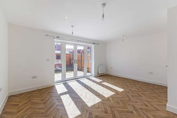 A room with a wooden floor and a white rug in front of a glass door.