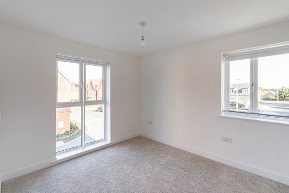 A room with a carpeted floor and two windows.