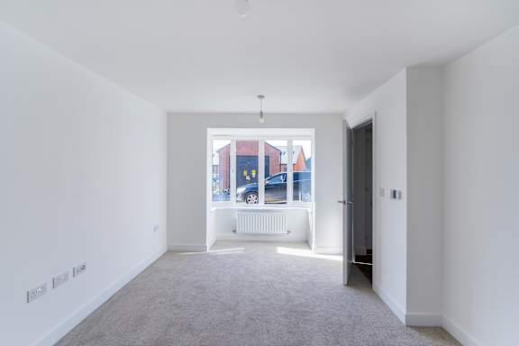 A room with white walls and a carpeted floor with a view of a street outside.