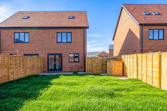 A red brick house with a wooden fence and green grass in front.