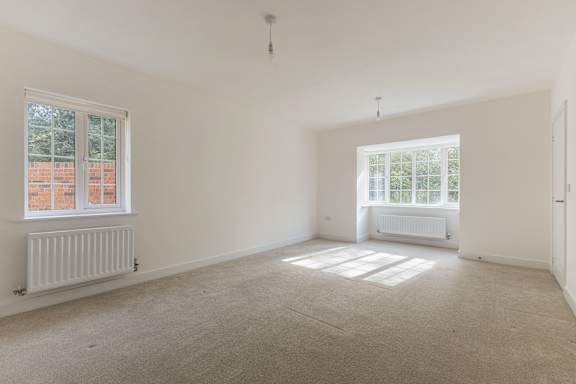 A large empty room with a window on the left and a radiator on the wall.