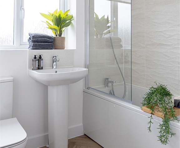 A white bathroom with a white toilet, a white sink, a white bathtub, and a white wall.